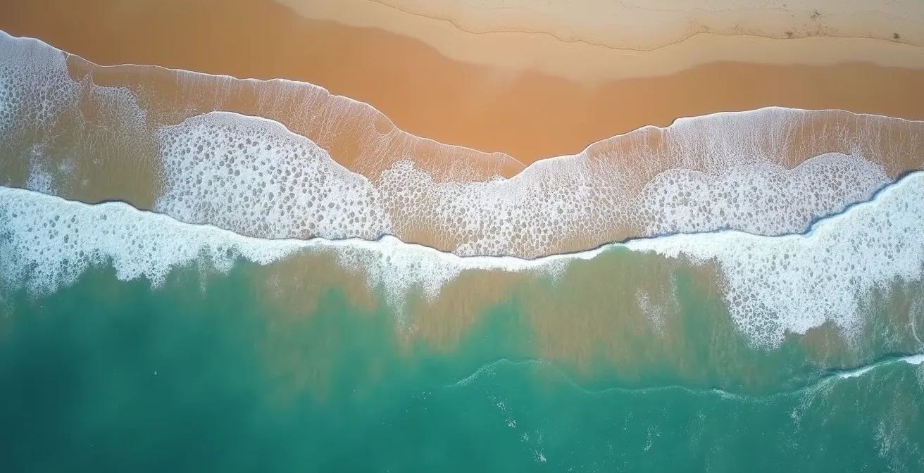Vue aérienne d'une baïne sur une plage atlantique montrant la zone calme et le canal d'eau qui s'éloigne vers le large entre les vagues.